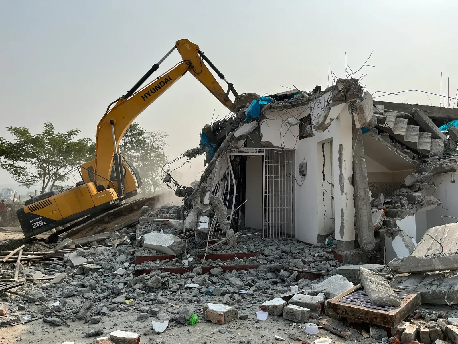 Excavator tearing down a partially demolished house