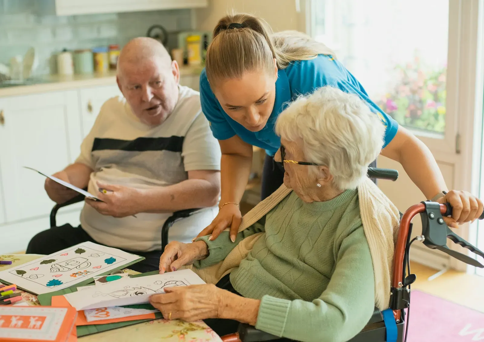 Caregiver helping an elderly woman in a wheelchair with a coloring activity