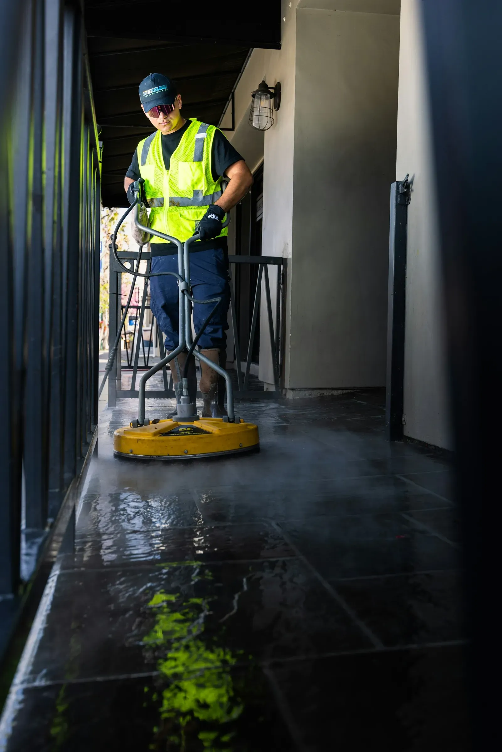 Cleaning crew member machine-scrubbing a tiled walkway