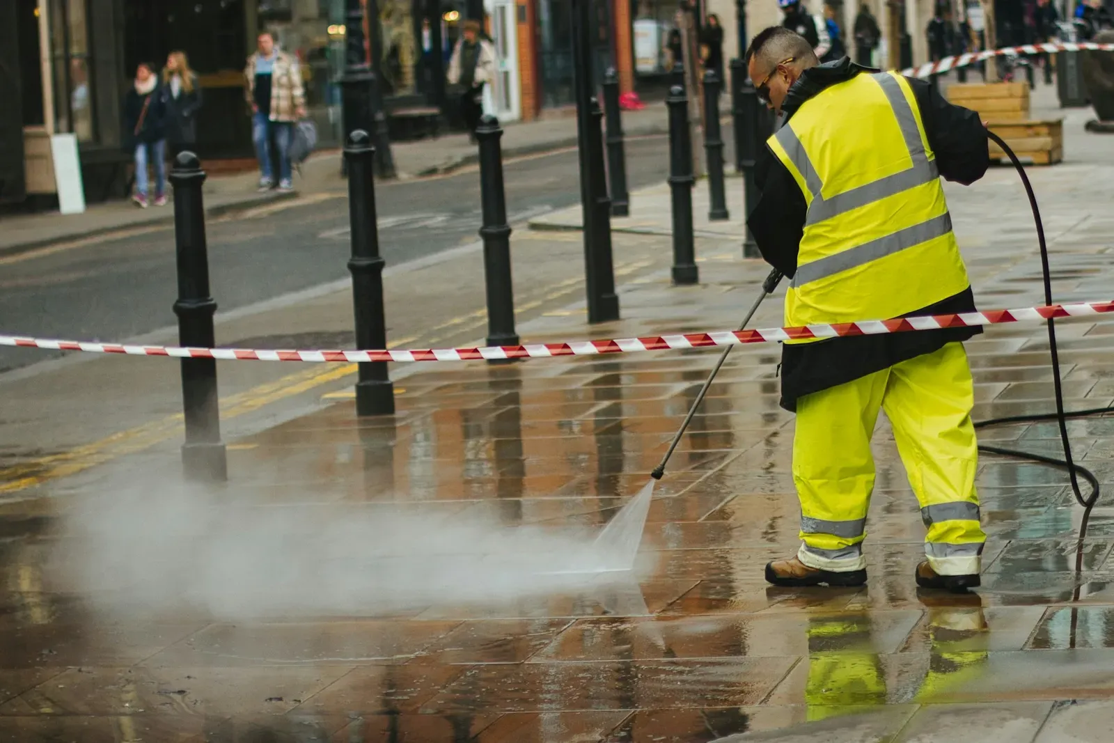 Worker in hi-vis pressure washing a sidewalk