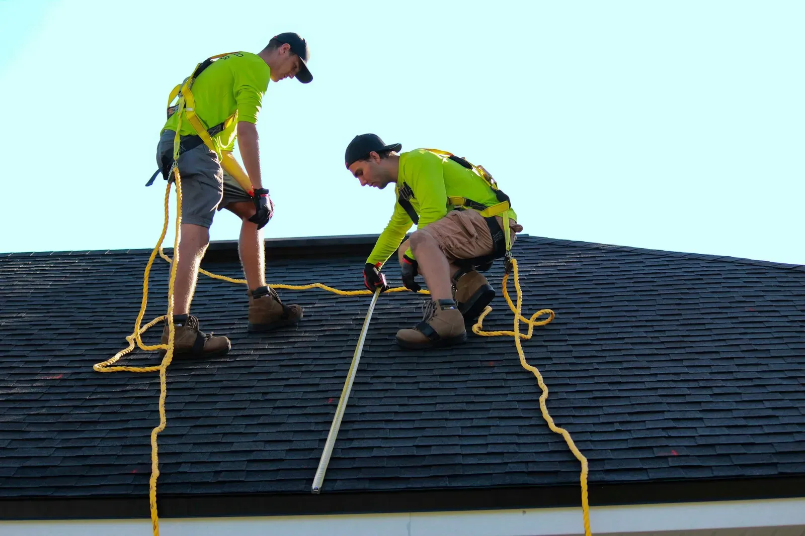 Two roofers in harnesses measuring an asphalt shingle roof